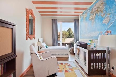 Child bedroom with a coral striped painted ceiling, world map wall, white crib, and armchair