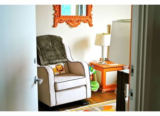 Reading corner with a cream armchair, orange side table, lamp, and patterned rug